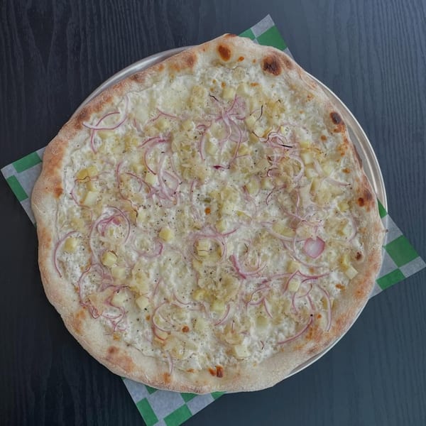 White pizza with diced potatoes and thinly sliced red onions on a metal pan.