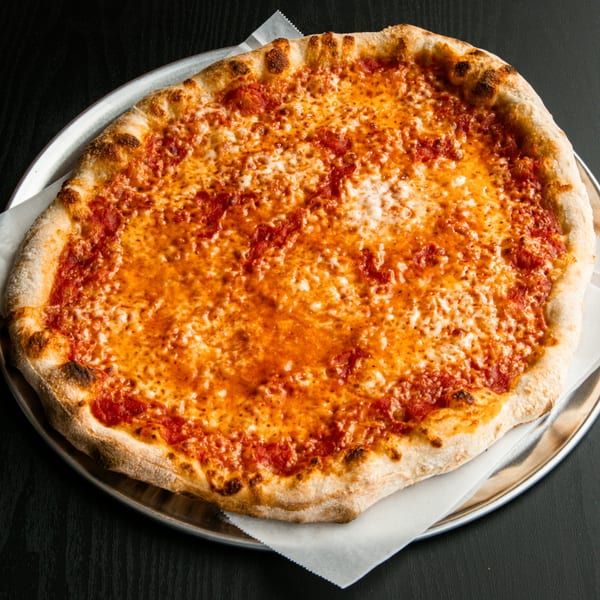 A whole cheese pizza with a golden crust sits on a metal tray with white parchment paper.