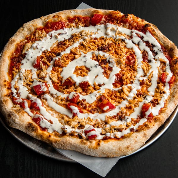 A whole buffalo chicken pizza with ranch dressing drizzled in a spiral pattern.