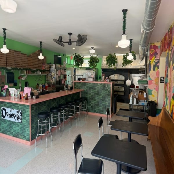 A vibrant restaurant interior with green walls, a pink and green tiled counter, and black tables.