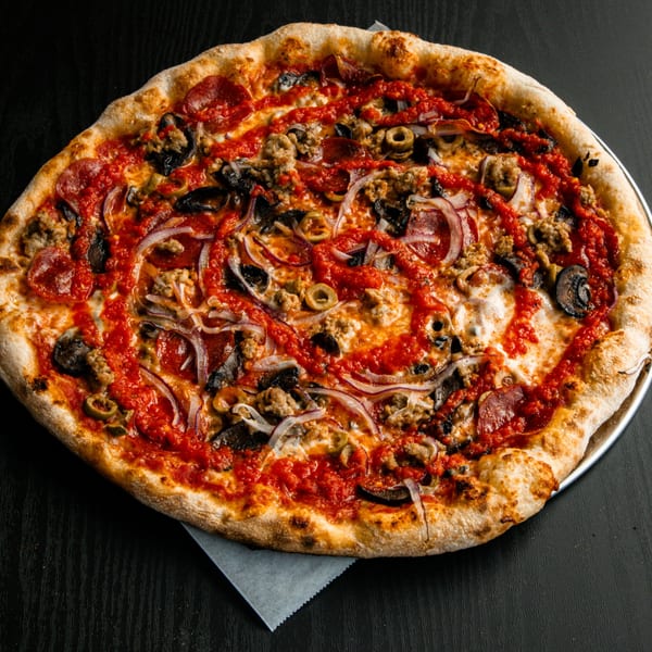 A whole pizza with pepperoni, sausage, mushrooms, olives, and red onions, drizzled with tomato sauce.