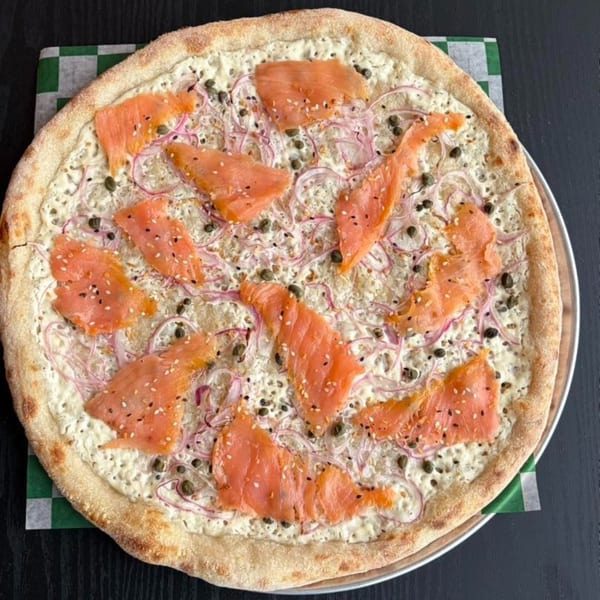 Smoked salmon pizza with white sauce, red onions, capers, and sesame seeds on a checkered paper.