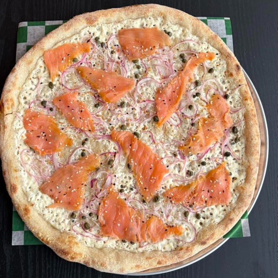 Smoked salmon pizza with white sauce, red onions, capers, and sesame seeds on a checkered paper.